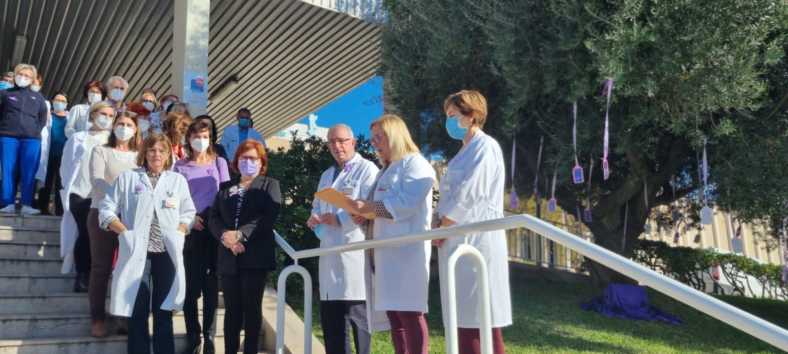 La directora de enfermería del departamento leyendo un manifiesto, en las escaleras de entrada al hospital, junto a al dirección del centro y los asistentes