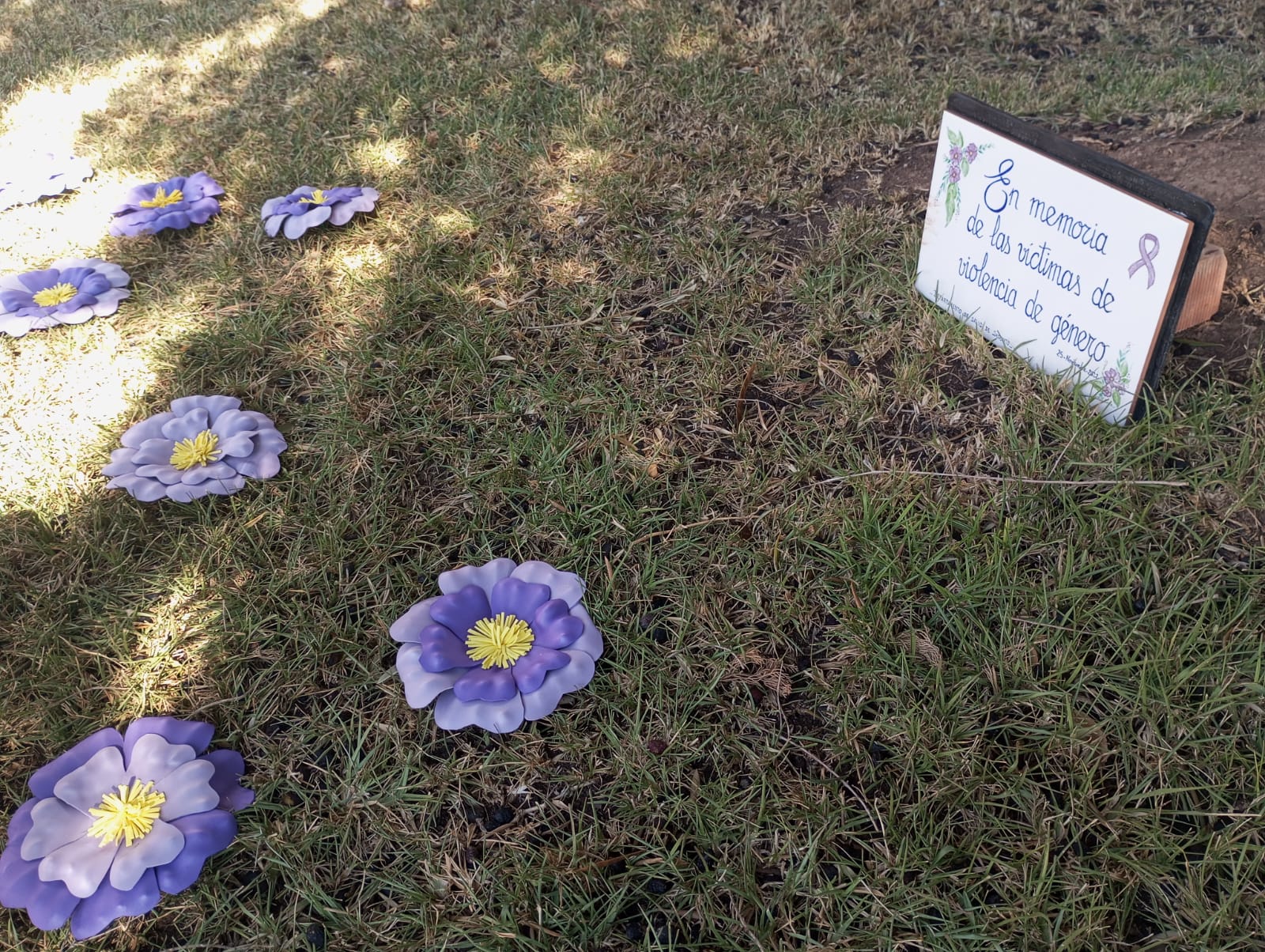 Fotos de papel clavadas en el suelo junto a placa conmemorativa por las víctimas 