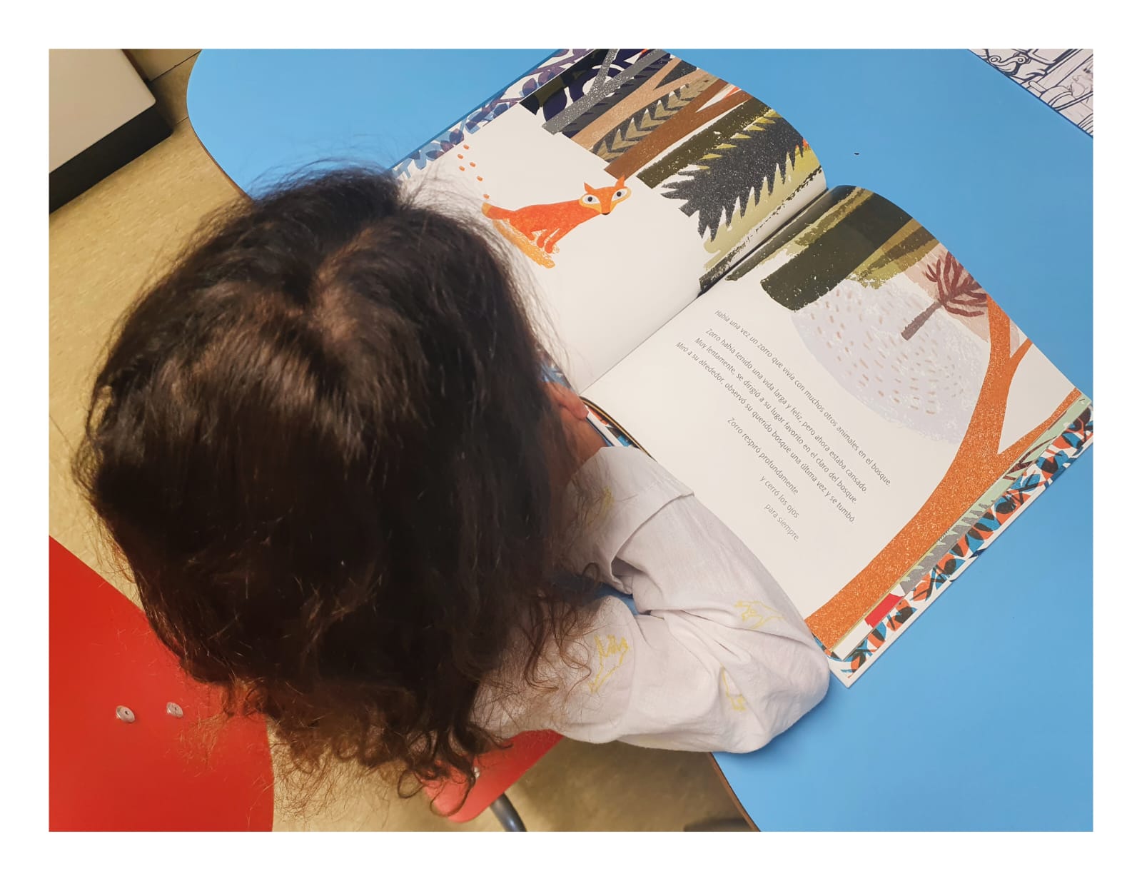 Una niña está sentada frente a su mesa de escritorio leyendo un libro con un dibujo de un zorro